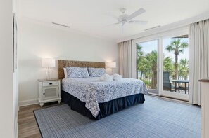 Een slaapkamer met een bed, nachtkastjes, een plafondventilator en uitzicht op palmbomen door een schuifdeur.