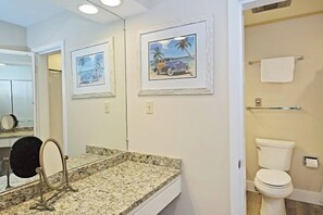 Un baño con encimera de granito, un espejo, un inodoro y cuadros en la pared.