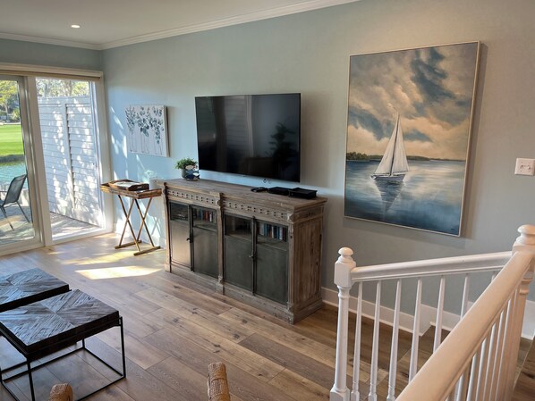 A spacious living room with a large TV, wooden flooring, and a view of the outdoors through sliding glass doors. - 189 Twin Oaks at The Sea Pines Resort (Hilton Head Island)