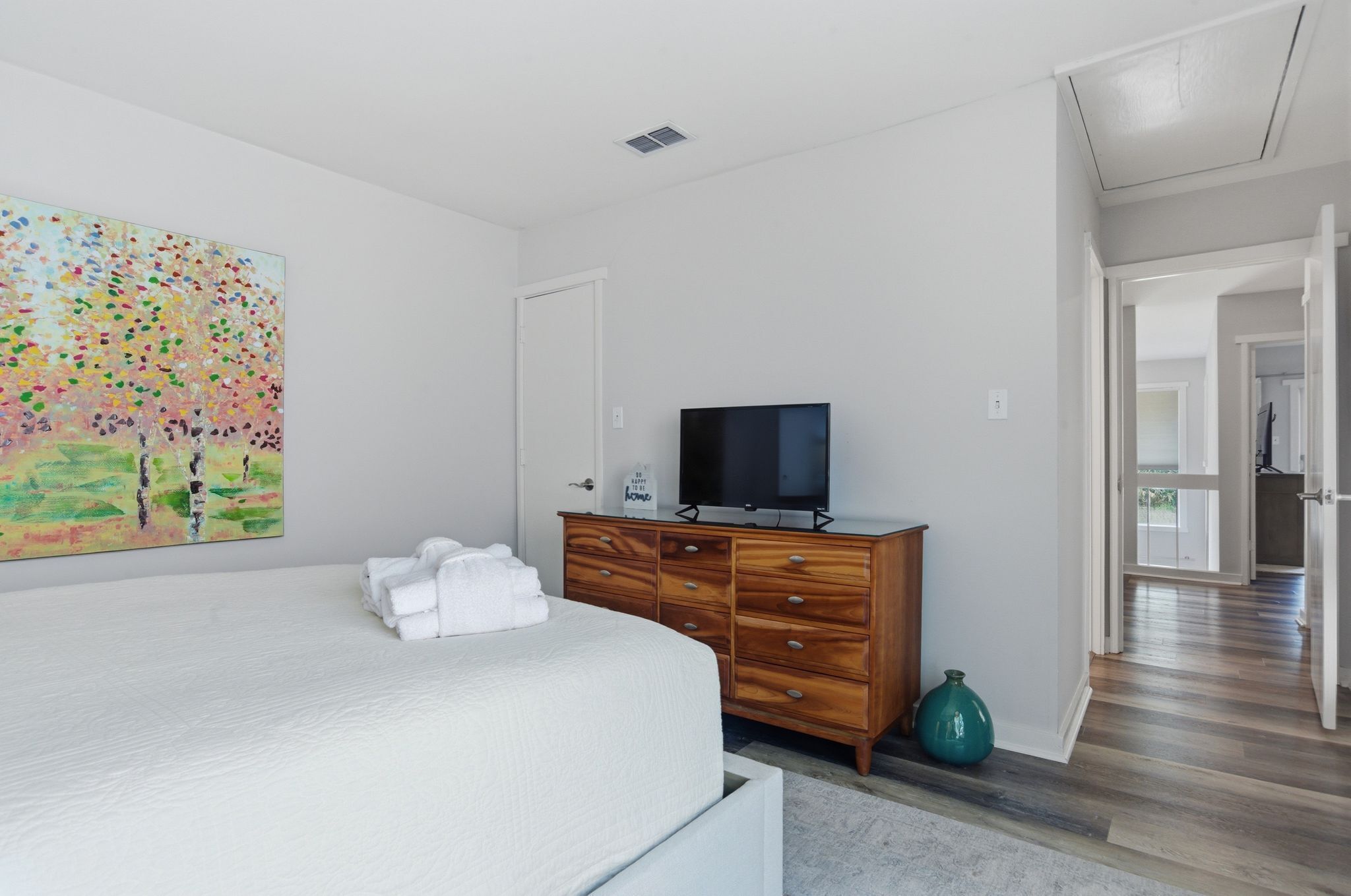 Un dormitorio con cama, cómoda, televisor y un cuadro en la pared.