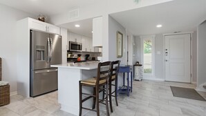 A modern kitchen with white cabinetry, stainless steel appliances, and a central island with bar stools.