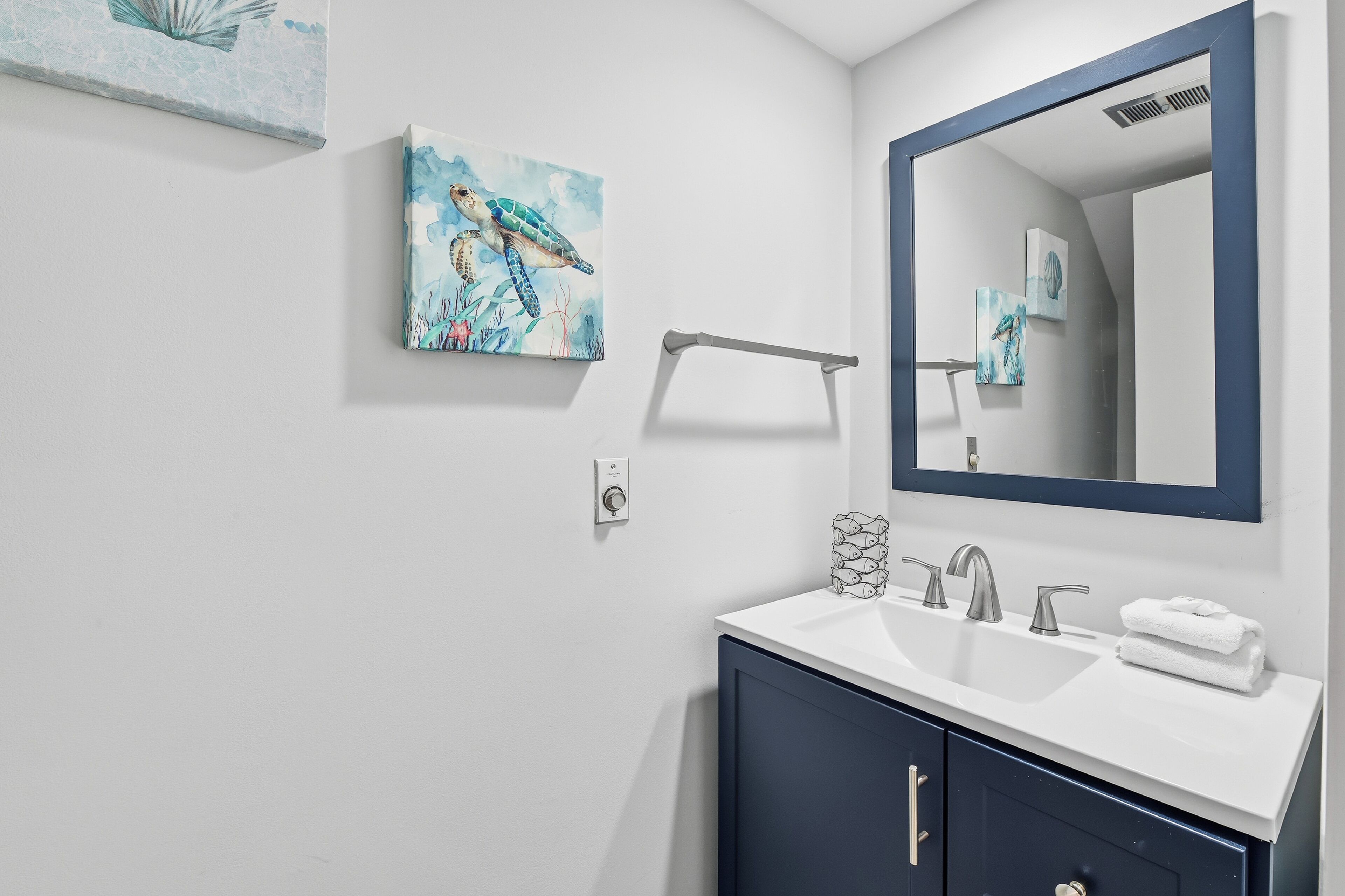 Een moderne badkamer met een witte wastafel, donkere kastjes en een grote spiegel. Twee kunstwerken aan de muur, afbeeldingen van zeeschildpadden.
