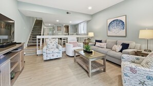 Amplia sala de estar con una escalera que conduce a un piso superior, un conjunto de sofás, una mesa de centro y un comedor.