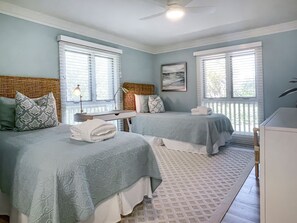 A room with two beds, a desk, and a ceiling fan.