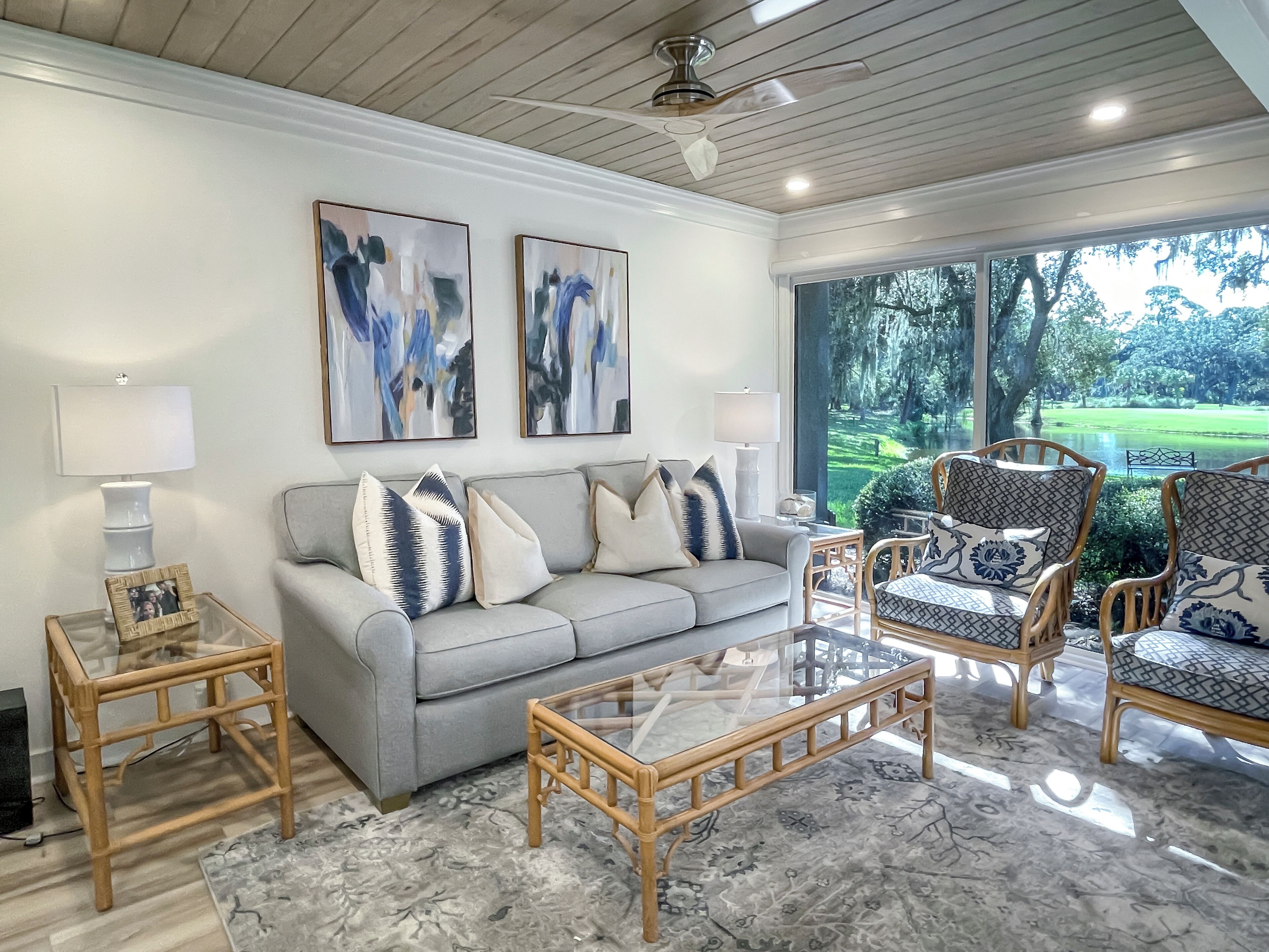 A living room with a grey sofa, patterned armchairs, a glass coffee table, and abstract art on the wall.