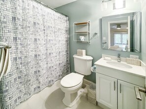 A bathroom with a patterned shower curtain, a toilet, a sink with a mirror, and a shelf with toiletries.
