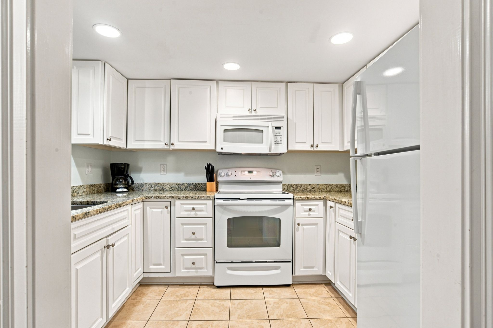 Una cocina con armarios blancos, microondas, estufa y refrigerador.