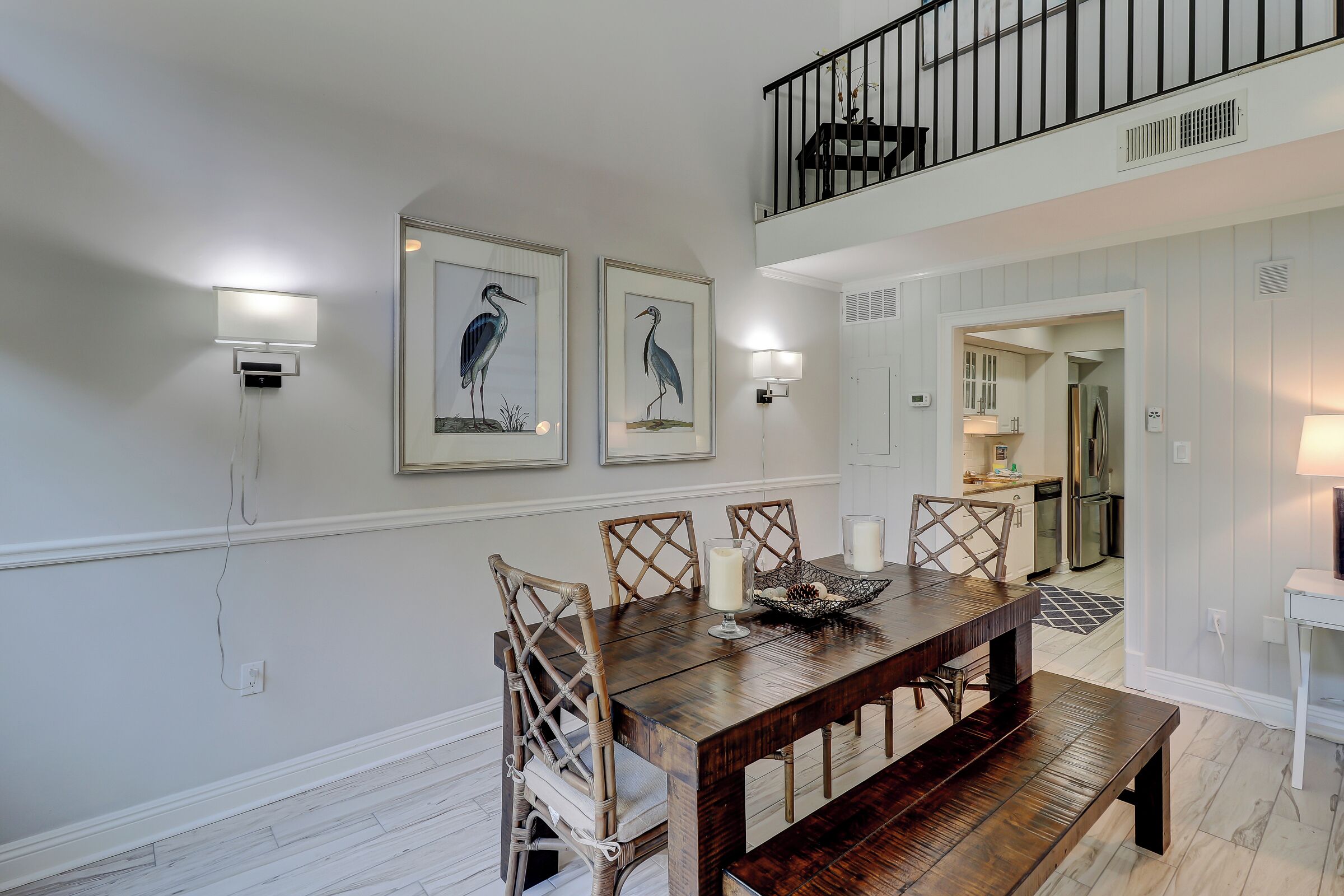 A dining area with a wooden table, wicker chairs, and wall-mounted light fixtures.