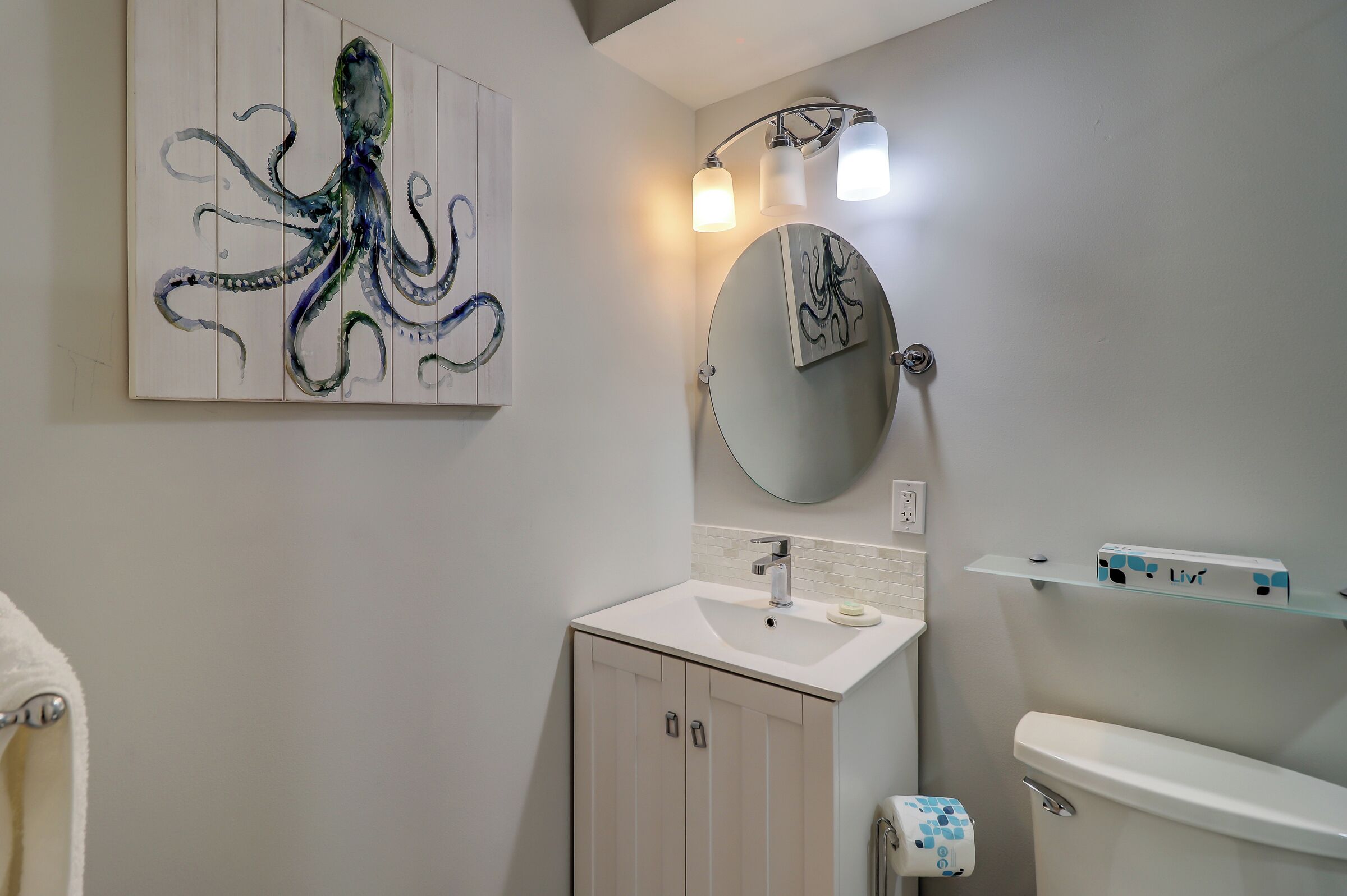 Une salle de bain avec un lavabo blanc, un miroir rond et un luminaire fixé au mur.