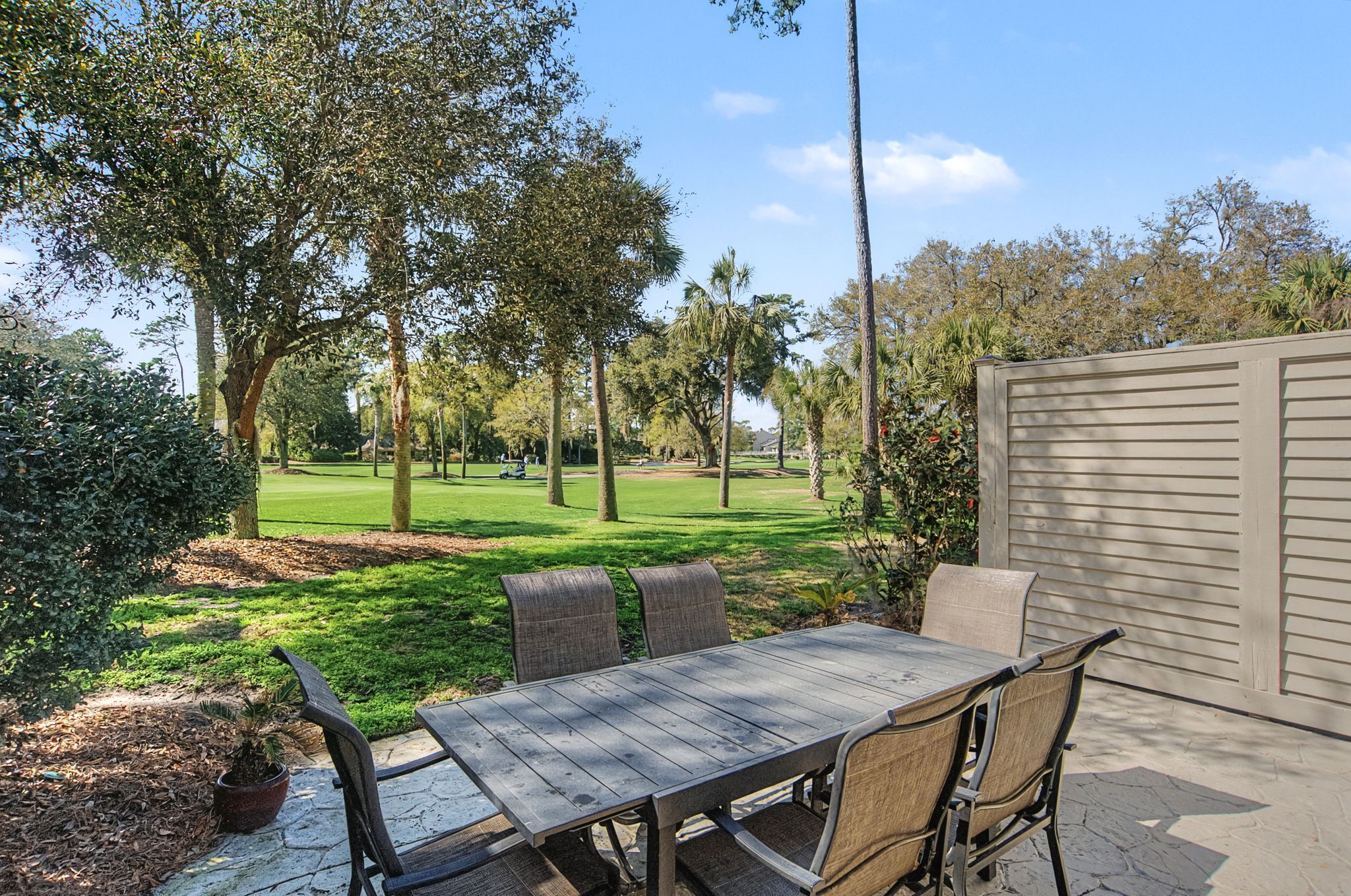 Um pátio com mesa e cadeiras, cercado por árvores e vista para um campo de golfe.