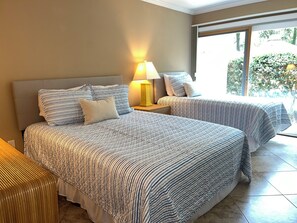 A hotel room with two beds, a nightstand with a lamp, and a view of greenery outside. - 153 Harbourwood Villa at The Sea Pines Resort (Hilton Head Island)