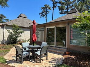A patio with a table and chairs, a red umbrella, and a sliding glass door. - 153 Harbourwood Villa at The Sea Pines Resort (Hilton Head Island)