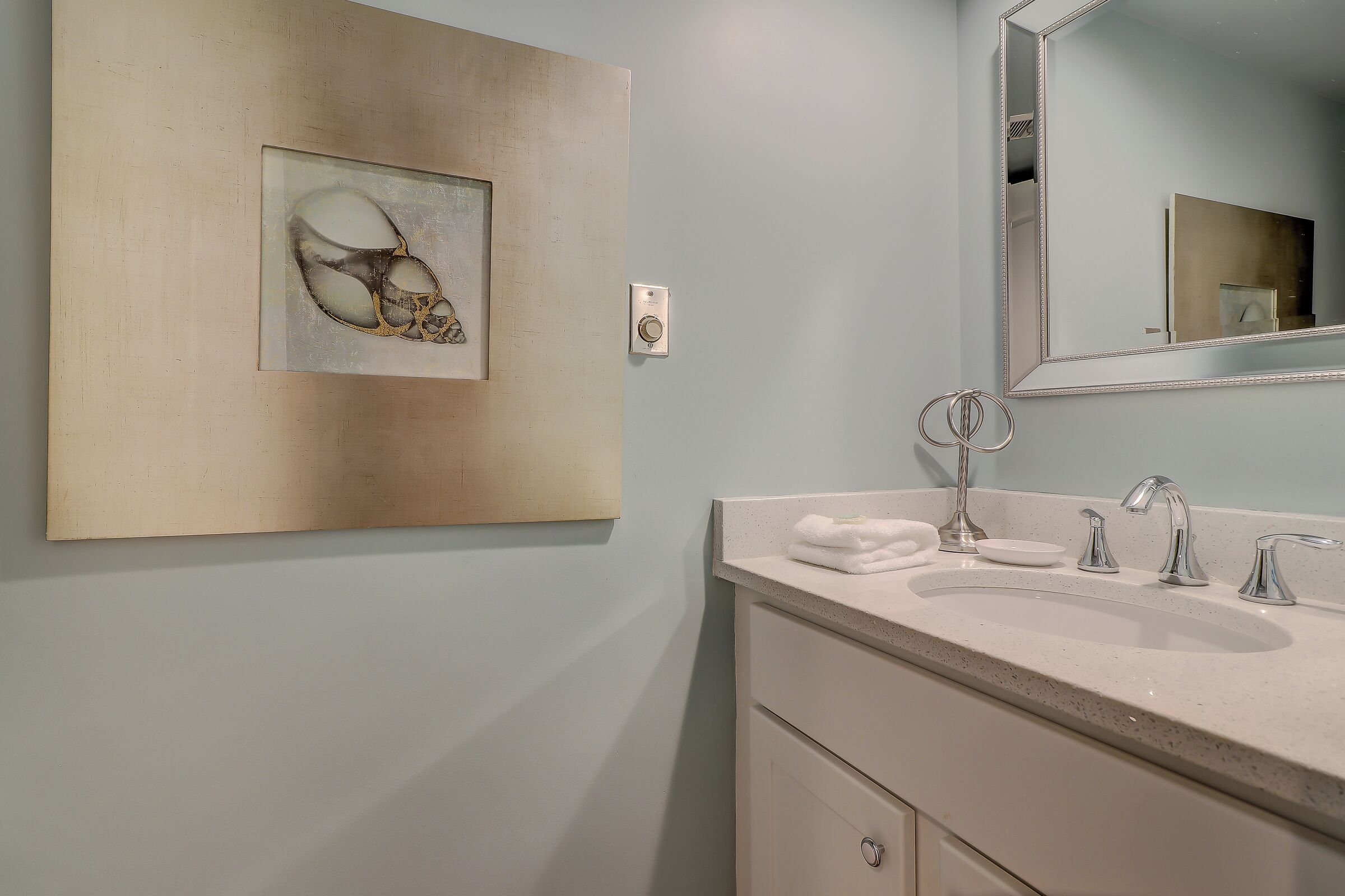 A bathroom with a large mirror, a sink with two faucets, and a towel on the counter.