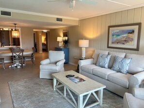 A living room with a sofa, armchairs, a coffee table, a dining area with a table and chairs, and a kitchen in the background.