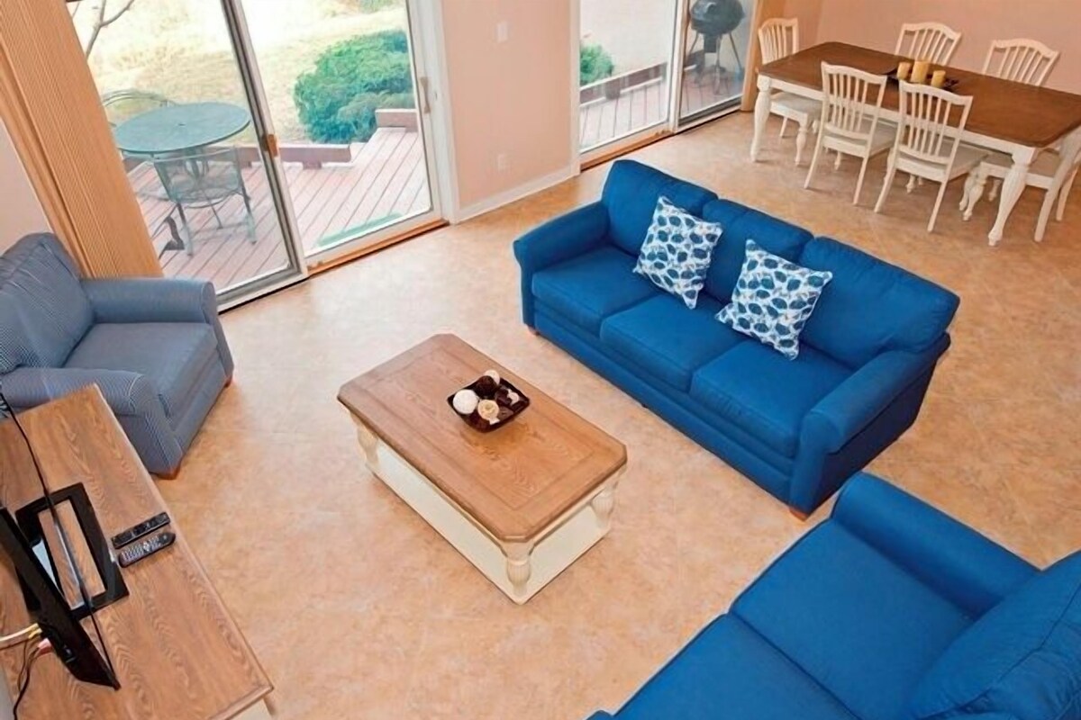 Una sala de estar con un sofá azul, una mesa de centro de madera y un mueble para la televisión.