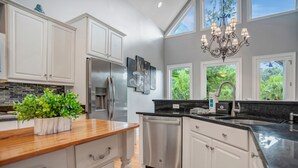 A modern kitchen with white cabinetry, a stainless steel refrigerator, a dishwasher, and a large window providing a view of greenery outside. - 64 Lawton Road at The Sea Pines Resort (Hilton Head Island)