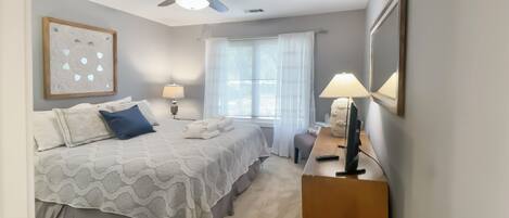 A neatly arranged bedroom with a bed, bedside lamps, a ceiling fan, and a window with curtains.