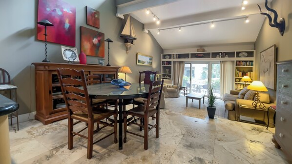 A dining area with a round table and wooden chairs, a bookshelf, and a view of the outside through a glass door. - 290 Stoney Creek Villa at The Sea Pines Resort (Hilton Head Island)