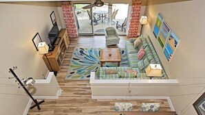 A modern living room with a sofa set, a coffee table, and a TV. There is a sliding glass door leading to an outdoor patio area.