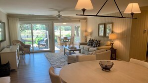 A spacious living area with a round dining table, comfortable seating, a sofa, and a view of the outdoors through large sliding doors.