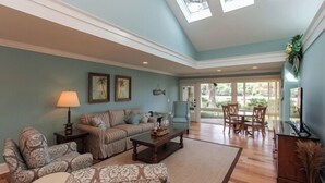 A spacious living room with a sofa set, a coffee table, and a TV. There is a dining area with a table and chairs. - 312 Beach Lagoon at The Sea Pines Resort (Hilton Head Island)
