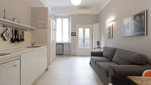 A modern kitchen with white cabinets, a grey sofa, and a dining table. - Italianway Comfort - Rosmini 13 D (Milan)