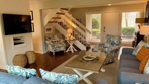 A living room with a staircase, a flat-screen TV mounted on the wall, and a sofa with patterned cushions. - 450 Plantation Club Villas at The Sea Pines Resort (Hilton Head Island)