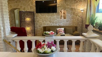 Eine Lounge mit Steinwänden, einem Flachbildfernseher über einer Couch, einem Wandkunstwerk und einem Geländer mit Blumen.