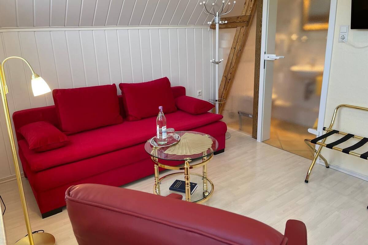 Un sofá rojo, una mesita redonda con tapa de vidrio, una lámpara de pie y un televisor montado en la pared.