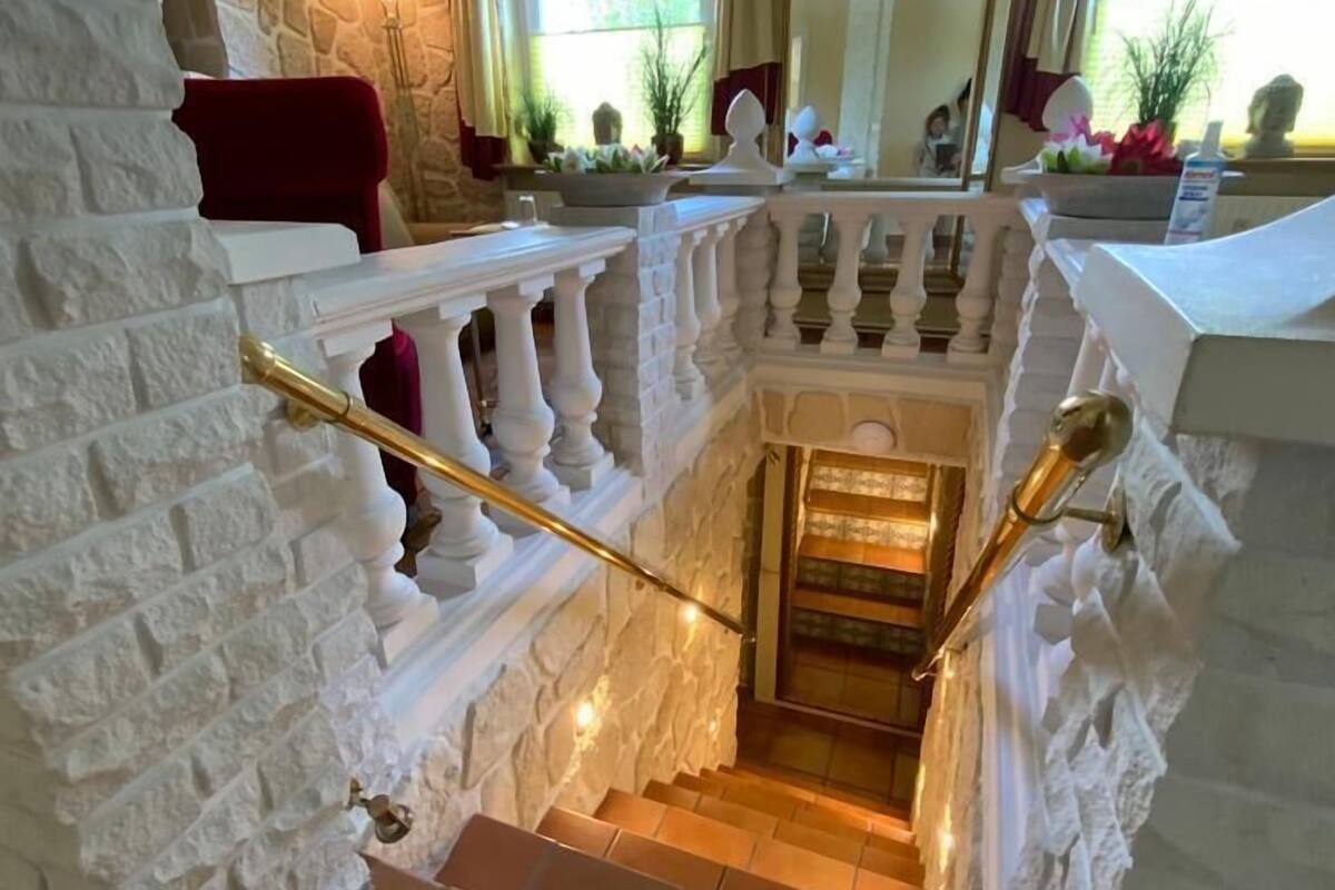 Una escalera con paredes de piedra blanca y barandilla, que desciende a un nivel inferior.