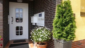 Un bâtiment en briques avec une porte blanche, une enseigne indiquant « Villa Vital » et deux plantes en pot.