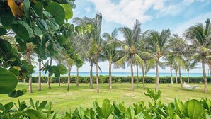 A tropical garden with palm trees and a view of the ocean. - Ocean Sun Pool Villas Resort Cam Ranh (Cam Lam)