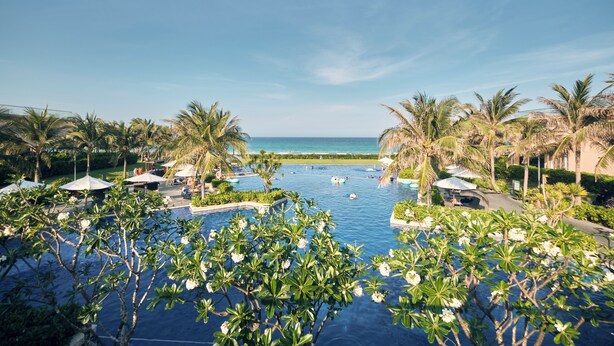 A pool area with palm trees and a view of the ocean. - Ocean Sun Pool Villas Resort Cam Ranh (Cam Lam)