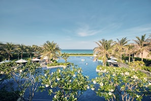 A pool area with palm trees and a view of the ocean. - Ocean Sun Pool Villas Resort Cam Ranh (Cam Lam)