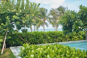 A pool surrounded by lush greenery and palm trees, with a view of the ocean. - Ocean Sun Pool Villas Resort Cam Ranh (Cam Lam)