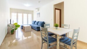 A modern living room with a sofa, a dining table with chairs, and a potted plant. - DREAM SEA APARTMENTS - 1 BEDROOM (El Ejido)