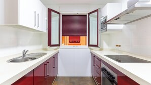A modern kitchen with white countertops, red cabinets, a central island, and a built-in oven. - DREAM SEA APARTMENTS - 1 BEDROOM (El Ejido)