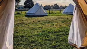 A view from inside a tent looking out at a grassy field with several yurts in the distance. - Nine Yards Bell Tents - Lytham (Lytham St. Anne's)