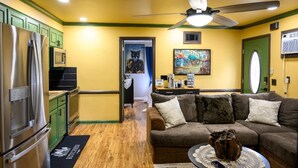 A compact living space with a kitchenette, a sofa, a ceiling fan, and a painting on the wall.