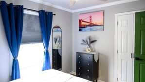 A bedroom with a bed, a dresser, a mirror, a ceiling fan, and a green door.