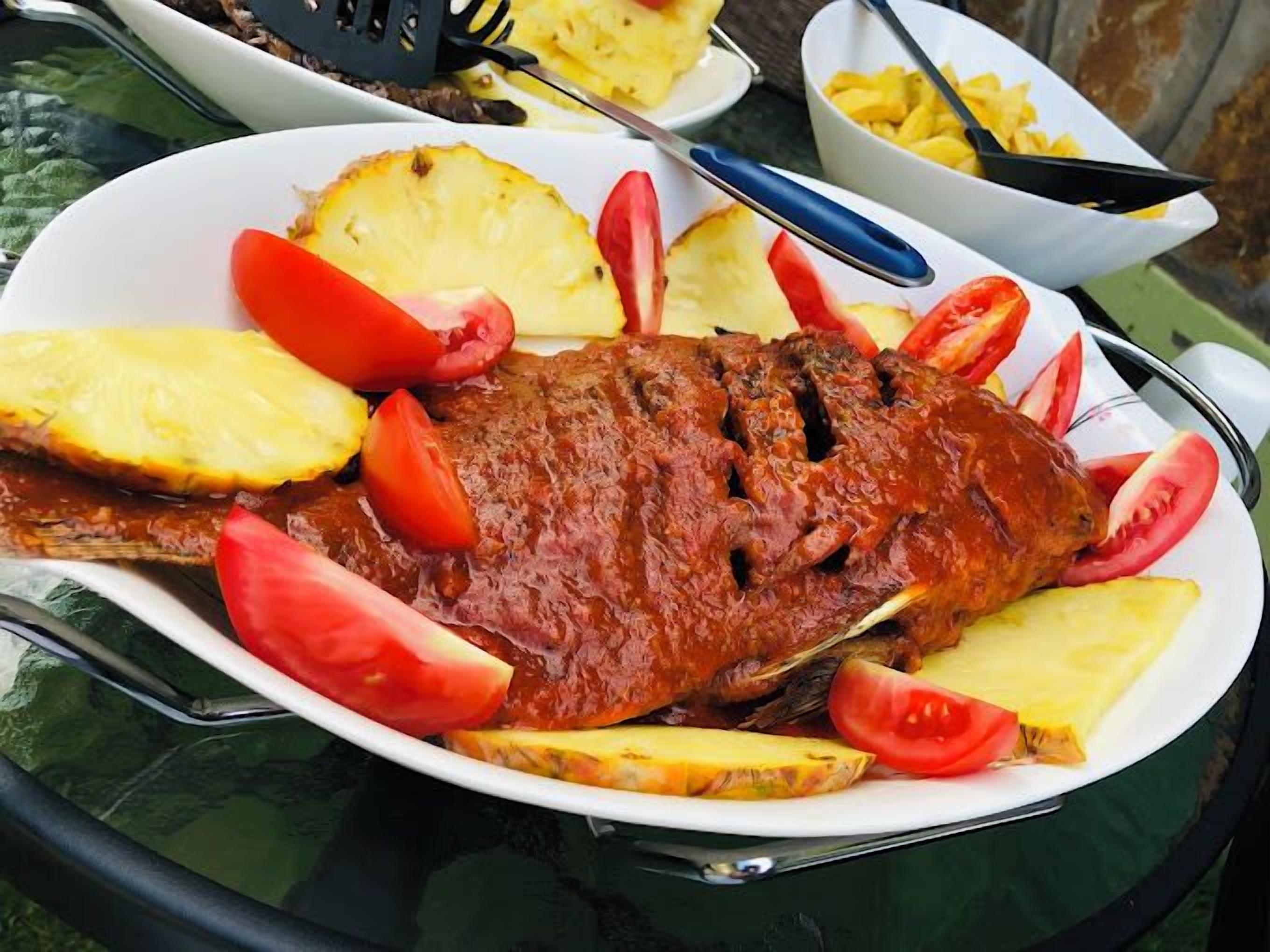 A plate with a grilled fish, pineapple slices, and tomato wedges.