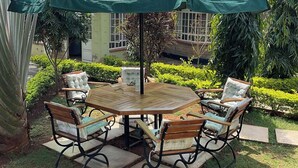An outdoor patio with a round wooden table and four cushioned chairs, surrounded by a green umbrella. - GreenHaven Siaya Cottages (Siaya)