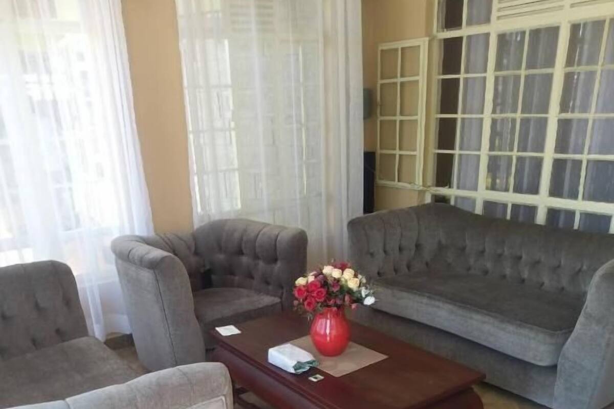 Un salon avec un canapé gris, des fauteuils, une table basse en bois et un vase de fleurs.