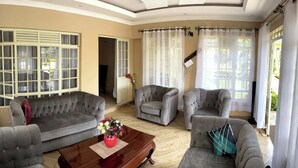 A spacious living room with a grey sofa set, a wooden coffee table, and a vase of flowers. - GreenHaven Siaya Cottages (Siaya)