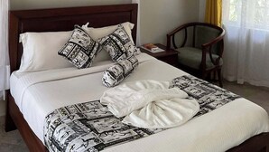 A neatly made bed with patterned bedding, a wooden headboard, and a bedside table with a book and a lamp. - GreenHaven Siaya Cottages (Siaya)
