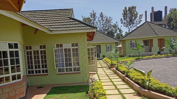 A building with a tiled roof, a paved pathway, and a garden with various plants. - GreenHaven Siaya Cottages (Siaya)