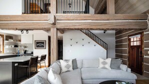Un espai de vida modern amb un sofà seccional en forma de L, una zona de cuina i una escala que porta a un nivell superior.
