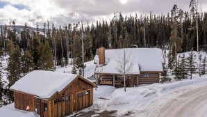 Una cabana de fusta amb un teulat cobert de neu, envoltada per un bosc i el terra ple de neu.