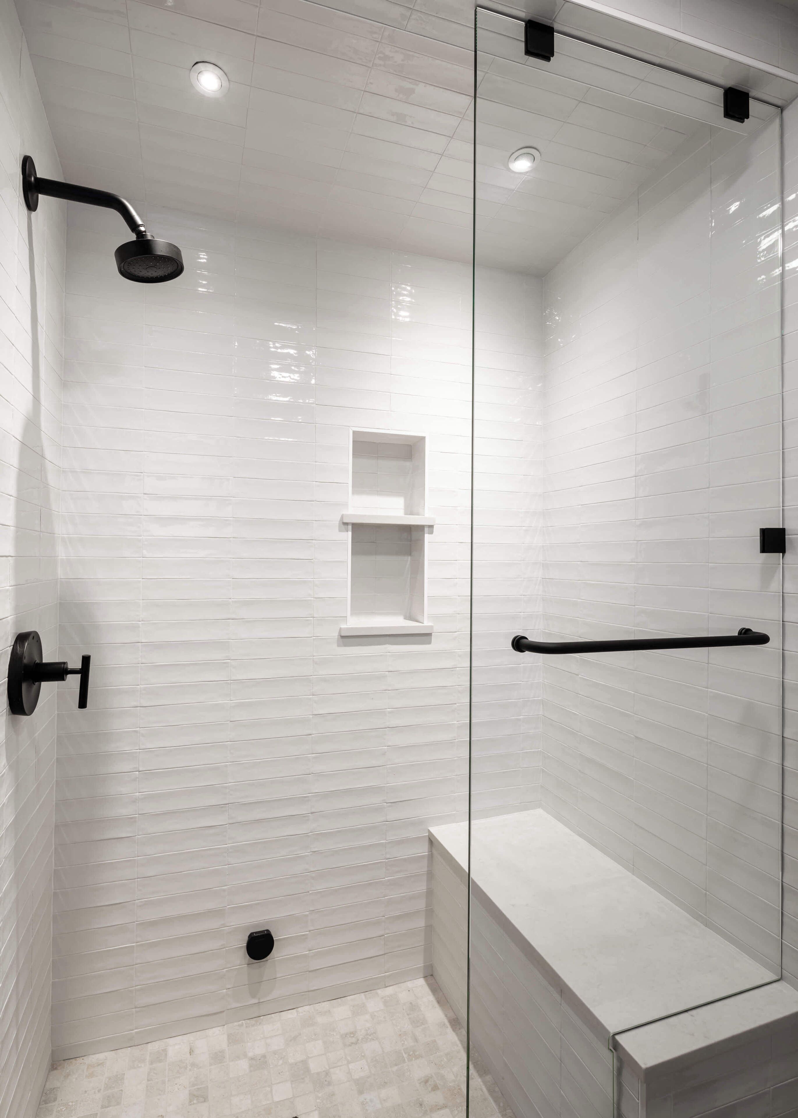 Une douche moderne avec une porte en verre, des murs recouverts de carreaux blancs et une porte-serviettes noire.