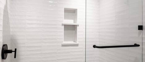Une douche moderne avec une porte en verre, des murs recouverts de carreaux blancs et une porte-serviettes noire.